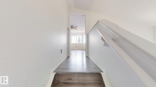 Wood-finish flooring throughout, bright white walls, and a white staircase with a classic handrail - 2426 33A Street Nw, Edmonton, AB - Indoor Photo Showing Other Room