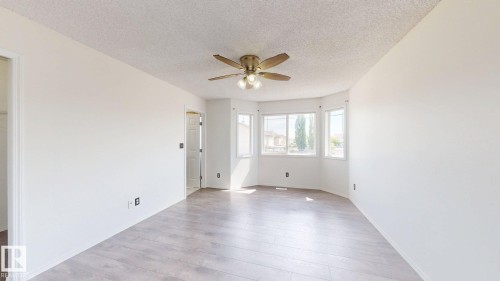 Expansive room featuring wood-finish flooring, a multi-pane bay window, and a ceiling fan with integrated lighting - 2426 33A Street Nw, Edmonton, AB - Indoor Photo Showing Other Room