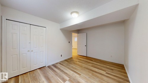 Wood-finish flooring, white bi-fold closet doors, and a ceiling-mounted light fixture - 2426 33A Street Nw, Edmonton, AB - Indoor Photo Showing Other Room
