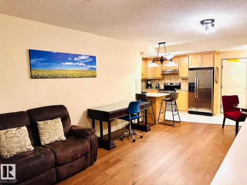 Hardwood-finish flooring throughout, kitchen featuring light wood cabinetry, stainless steel refrigerator, and tiled backsplash - #207 10142 111 St Nw, Edmonton, AB - Indoor