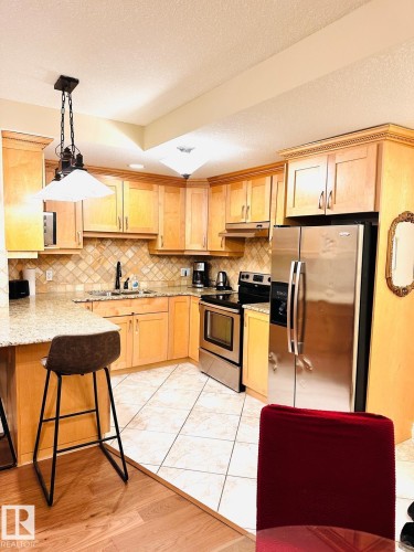 Kitchen featuring wood-finish cabinetry, stainless steel appliances, granite-style countertops, and a decorative tile backsplash - #207 10142 111 St Nw, Edmonton, AB - Indoor Photo Showing Kitchen