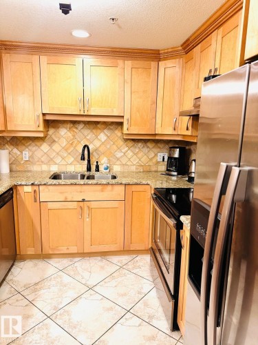 Recessed lighting illuminates wood cabinetry with crown molding, complemented by a tile backsplash and light-toned countertops - #207 10142 111 St Nw, Edmonton, AB - Indoor Photo Showing Kitchen With Double Sink