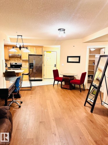 Wood-finish flooring throughout, stainless steel refrigerator, light wood cabinetry, tiled kitchen backsplash, and built-in shelving - #207 10142 111 St Nw, Edmonton, AB - Indoor