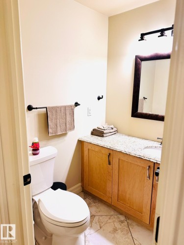 Vanity with a granite-style countertop, wood-finish cabinetry, and a framed mirror - #207 10142 111 St Nw, Edmonton, AB - Indoor Photo Showing Bathroom