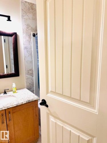 Wood-finish vanity with a light-colored countertop, undermount sink, and dark-toned faucet - #207 10142 111 St Nw, Edmonton, AB - Indoor Photo Showing Bathroom