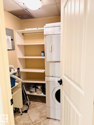 Stackable laundry appliances, integrated shelving, tiled flooring, paneled interior door - #207 10142 111 St Nw, Edmonton, AB - Indoor Photo Showing Laundry Room