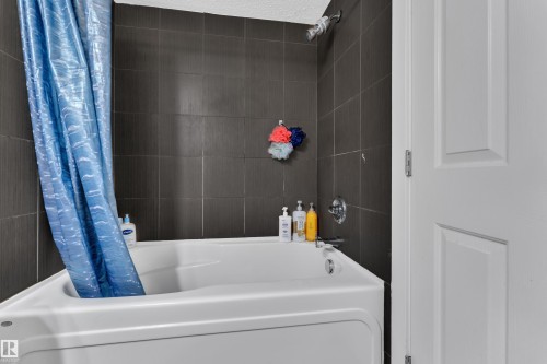 White tub and shower combination with dark tile surround and chrome fixtures - #409 11804 22 Av Sw, Edmonton, AB - Indoor Photo Showing Bathroom