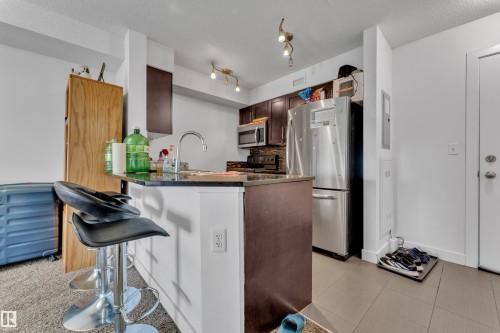 Kitchen featuring dark wood-finish cabinetry, stainless steel appliances, a black granite countertop, and a tile backsplash - #409 11804 22 Av Sw, Edmonton, AB - Indoor Photo Showing Kitchen