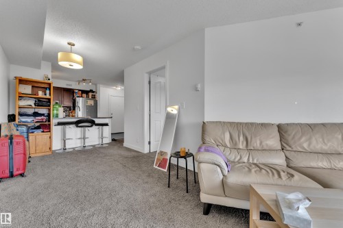 Open-concept living area featuring a kitchen with a breakfast bar, stainless steel refrigerator, and dark wood-finish cabinetry - #409 11804 22 Av Sw, Edmonton, AB - Indoor Photo Showing Living Room
