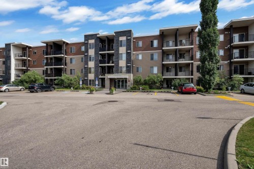 Contemporary multi-story building featuring exterior balconies, stone facade accents, and a paved parking area - #409 11804 22 Av Sw, Edmonton, AB - Outdoor With Balcony With Facade