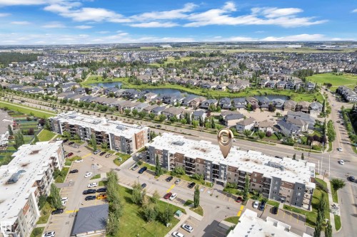 Aerial perspective showcasing a multi-story residential building within a developed community, featuring surface parking, green spaces, and surrounding residential areas with ponds - #409 11804 22 Av Sw, Edmonton, AB - Outdoor With View