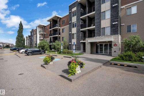 Multi-story building with a stone facade entrance, individual balconies with black railings, and a paved parking area - #409 11804 22 Av Sw, Edmonton, AB - Outdoor With Balcony With Facade
