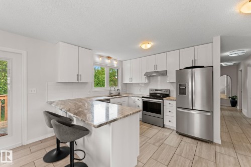 Modern kitchen featuring white cabinetry, stainless steel appliances, a tiled backsplash, and light-toned countertops with a breakfast bar - 34 Stirling Road Nw, Edmonton, AB - Indoor Photo Showing Kitchen With Upgraded Kitchen