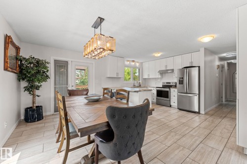 Open-concept kitchen and dining area featuring light-toned tile flooring, white cabinetry, stainless steel appliances, and a central island with countertop seating - 34 Stirling Road Nw, Edmonton, AB - Indoor Photo Showing Other Room