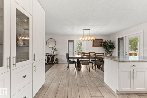 Open-concept living space featuring wood-finish flooring, white cabinetry with glass-front uppers, and a dining area with a linear chandelier - 34 Stirling Road Nw, Edmonton, AB - Indoor Photo Showing Dining Room