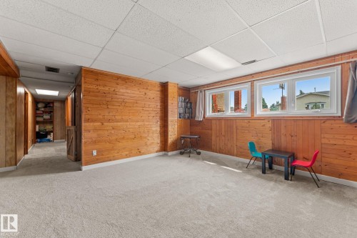 Spacious carpeted room featuring extensive wood paneling and two large windows - 34 Stirling Road Nw, Edmonton, AB - Indoor Photo Showing Other Room