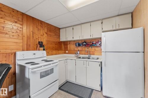 Kitchen featuring wood-panel walls, white cabinetry, light countertops, a double basin sink, and white appliances - 34 Stirling Road Nw, Edmonton, AB - Indoor Photo Showing Kitchen With Double Sink