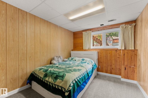 Carpeted room featuring wood-finish paneling, a drop ceiling with recessed lighting, and a window with a built-in wood-finish cabinet below - 34 Stirling Road Nw, Edmonton, AB - Indoor Photo Showing Bedroom