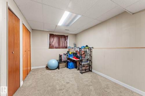 Carpeted room featuring two wood-finish bi-fold doors and a drop ceiling with recessed lighting - 34 Stirling Road Nw, Edmonton, AB - Indoor