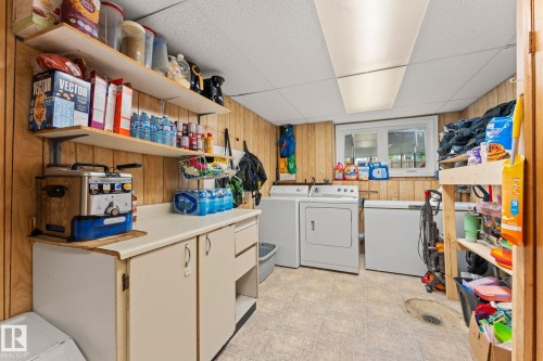 Utility room featuring a window, built-in cabinetry, wall shelving, and a drop ceiling - 34 Stirling Road Nw, Edmonton, AB - Indoor Photo Showing Laundry Room