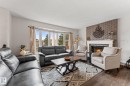 Living area with wood-finish flooring, a prominent bay window, and a brick-accented fireplace featuring a white mantel - 34 Stirling Road Nw, Edmonton, AB  - Indoor Photo Showing Living Room With Fireplace 