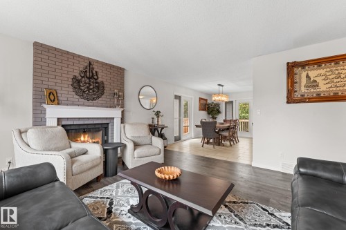Living area featuring a brick-surround fireplace with a white mantel, wood-finish flooring, and recessed lighting - 34 Stirling Road Nw, Edmonton, AB - Indoor Photo Showing Living Room With Fireplace
