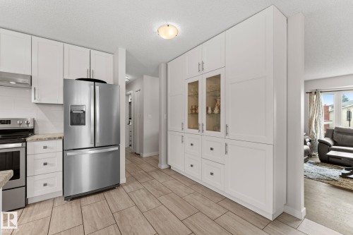 Kitchen featuring white cabinetry, stainless steel appliances, a tiled backsplash, and wood-finish flooring - 34 Stirling Road Nw, Edmonton, AB - Indoor Photo Showing Kitchen