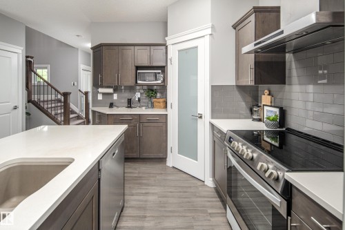 Modern kitchen featuring wood-finish flooring, stainless steel appliances, white countertops, and a gray subway tile backsplash - 16015 11 Avenue Sw, Edmonton, AB - Indoor Photo Showing Kitchen