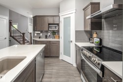 Modern kitchen featuring wood-finish flooring, stainless steel appliances, white countertops, and a gray subway tile backsplash - 