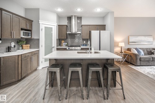 Open-concept kitchen featuring wood-finish flooring, white countertops, built-in stainless steel appliances, and a central island with integrated seating - 16015 11 Avenue Sw, Edmonton, AB - Indoor Photo Showing Kitchen