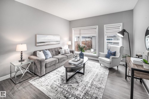 Wood-finish flooring throughout, light gray wall paint, and two large windows with blinds - 16015 11 Avenue Sw, Edmonton, AB - Indoor Photo Showing Living Room