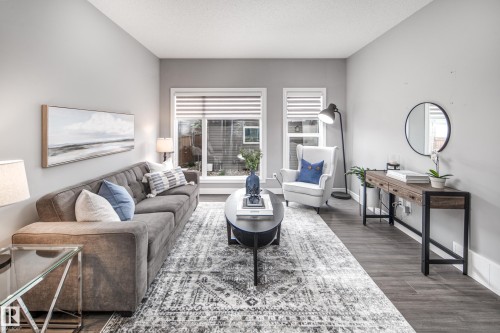 Recessed lighting illuminates the living area featuring wood-finish flooring, white window blinds, and a built-in wall mirror - 16015 11 Avenue Sw, Edmonton, AB - Indoor Photo Showing Living Room