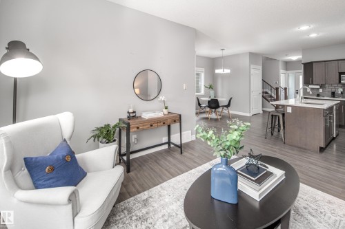 Open-concept living space featuring wood-finish flooring, a kitchen island with seating, dark wood cabinetry, a tiled kitchen backsplash, and a dining area - 16015 11 Avenue Sw, Edmonton, AB - Indoor