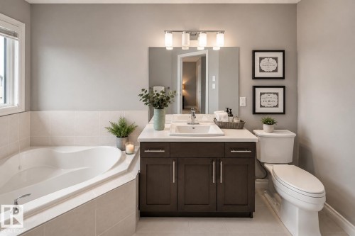 Corner soaking tub with tiled surround, single vanity with integrated sink, dark wood-finish cabinetry, and overhead vanity lighting - 16015 11 Avenue Sw, Edmonton, AB - Indoor Photo Showing Bathroom
