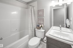 White shower-tub combination, single vanity with integrated sink, chrome faucet, and gray wood-finish cabinetry - 