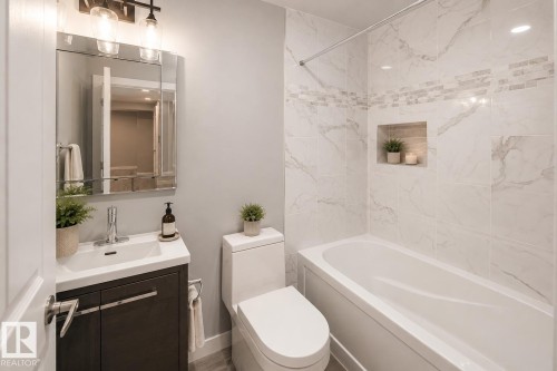 Vanity with integrated sink, sleek chrome faucet, framed medicine cabinet, built-in tub with tile surround, and recessed shower niche - 16015 11 Avenue Sw, Edmonton, AB - Indoor Photo Showing Bathroom