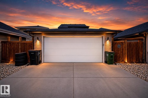 Concrete driveway with integrated lighting, wood fencing, and a white garage door - 16015 11 Avenue Sw, Edmonton, AB - Outdoor With Exterior