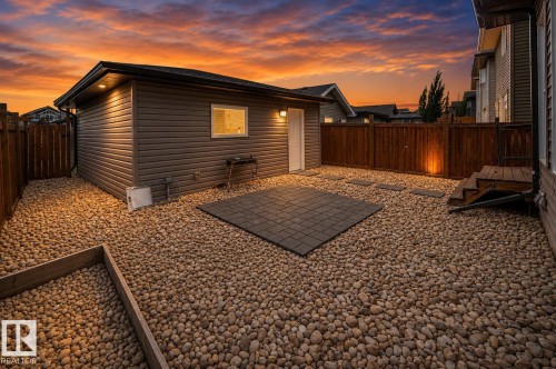 Spacious backyard retreat featuring a detached studio with illuminated interior, gravel landscaping with metal edging, composite patio pad, and wooden privacy fencing - 16015 11 Avenue Sw, Edmonton, AB - Outdoor