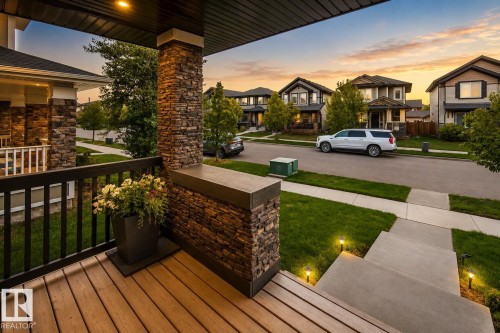 Inviting front porch with wood-finish decking and stone veneer columns - 16015 11 Avenue Sw, Edmonton, AB - Outdoor With Exterior
