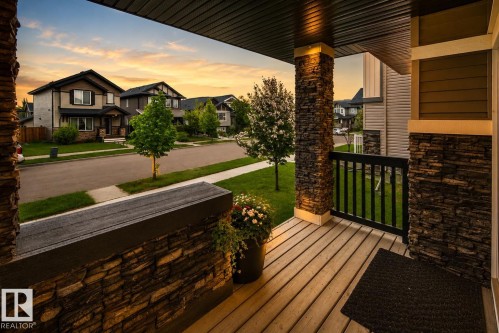 Inviting front porch featuring wood-finish decking, stone-clad pillars, and a black spindle railing - 16015 11 Avenue Sw, Edmonton, AB - Outdoor With Deck Patio Veranda