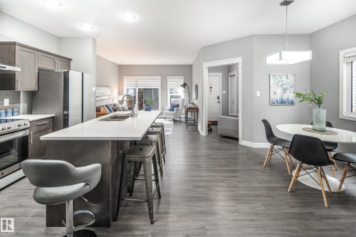 Open-concept living area featuring wood-finish flooring, a kitchen island with seating, stainless steel appliances, and recessed lighting - 16015 11 Avenue Sw, Edmonton, AB - Indoor