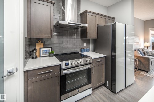 Kitchen featuring stainless steel appliances, dark wood-finish cabinetry, light-toned countertops, and a gray subway tile backsplash - 16015 11 Avenue Sw, Edmonton, AB - Indoor Photo Showing Kitchen