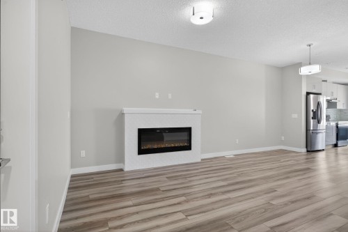Open-concept living area with wood-finish flooring, a contemporary electric fireplace, and recessed ceiling lighting - 4879 Alwood Point(E) Sw, Edmonton, AB - Indoor With Fireplace