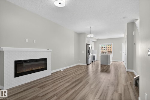 Electric fireplace with tiled surround, wood-finish flooring, recessed lighting, and a kitchen island - 4879 Alwood Point(E) Sw, Edmonton, AB - Indoor Photo Showing Living Room With Fireplace