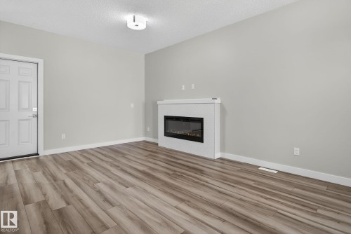 Wood-finish flooring, white paneled door, and a built-in electric fireplace with a patterned white surround - 4879 Alwood Point(E) Sw, Edmonton, AB - Indoor Photo Showing Living Room With Fireplace