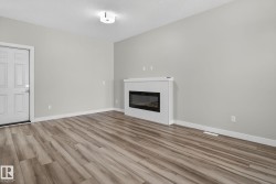 Wood-finish flooring, white paneled door, and a built-in electric fireplace with a patterned white surround - 