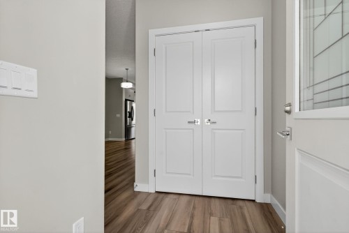 Wood-finish flooring with white baseboards, white double doors with brushed nickel hardware, and a white entry door with frosted glass detailing - 4879 Alwood Point(E) Sw, Edmonton, AB - Indoor Photo Showing Other Room