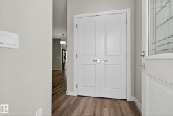 Wood-finish flooring with white baseboards, white double doors with brushed nickel hardware, and a white entry door with frosted glass detailing - 