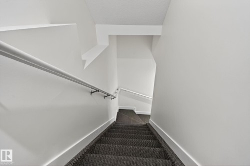 Stairwell featuring a carpeted staircase, white handrail with metal brackets, and white painted walls - 4879 Alwood Point(E) Sw, Edmonton, AB - Indoor
