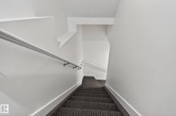 Stairwell featuring a carpeted staircase, white handrail with metal brackets, and white painted walls - 